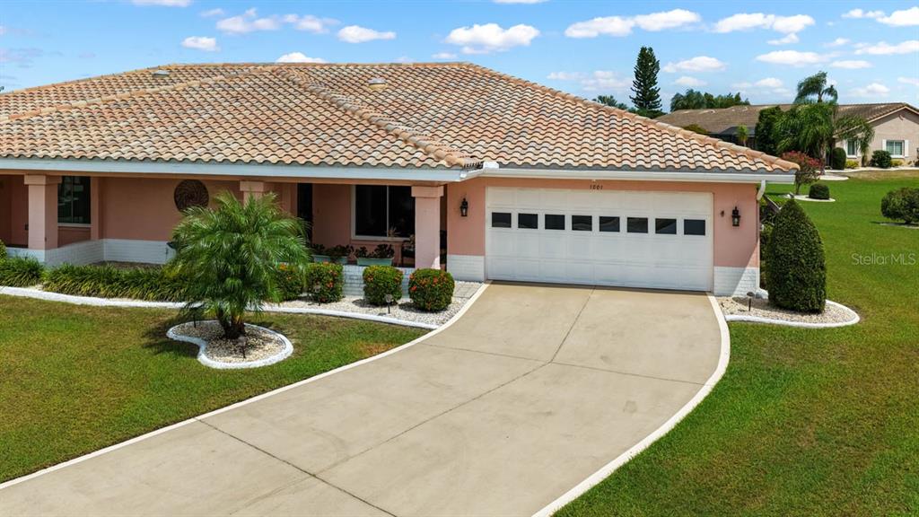 A single-story peach-colored house features a tiled roof, a two-car garage, and a concrete driveway — 1001 ARDMORE WAY, SUN CITY CENTER, FL