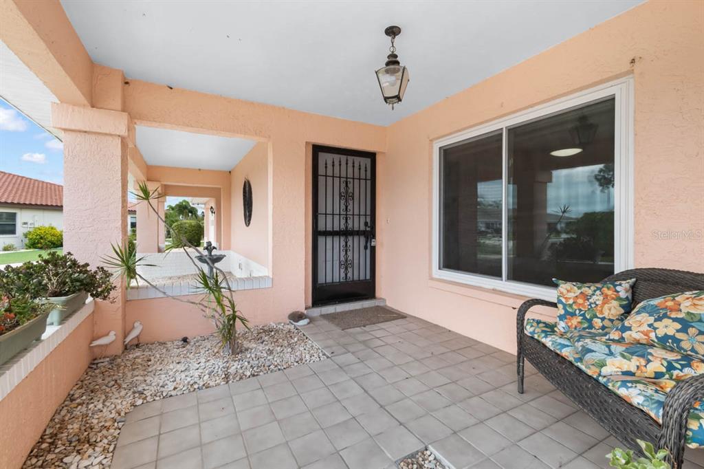 A covered patio features tiled flooring, a decorative metal security door, and a wicker bench — 1001 ARDMORE WAY, SUN CITY CENTER, FL