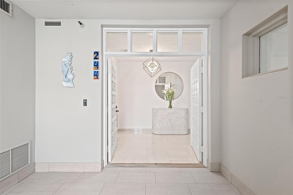 A bright entryway features white tile floors, a decorative seahorse, and a glass-paneled double door — 2450 HARBOURSIDE DRIVE UNIT 244, LONGBOAT KEY, FL