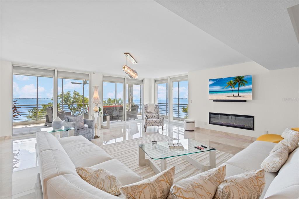 A bright living room features a white sectional, glass coffee table, fireplace, and waterfront balcony views — 2450 HARBOURSIDE DRIVE UNIT 244, LONGBOAT KEY, FL