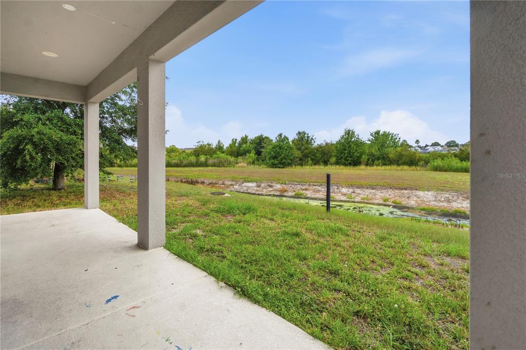 A covered concrete patio overlooks a grassy yard, a drainage ditch, and a treeline — 205 ABERDEEN STREET, DAVENPORT, FL