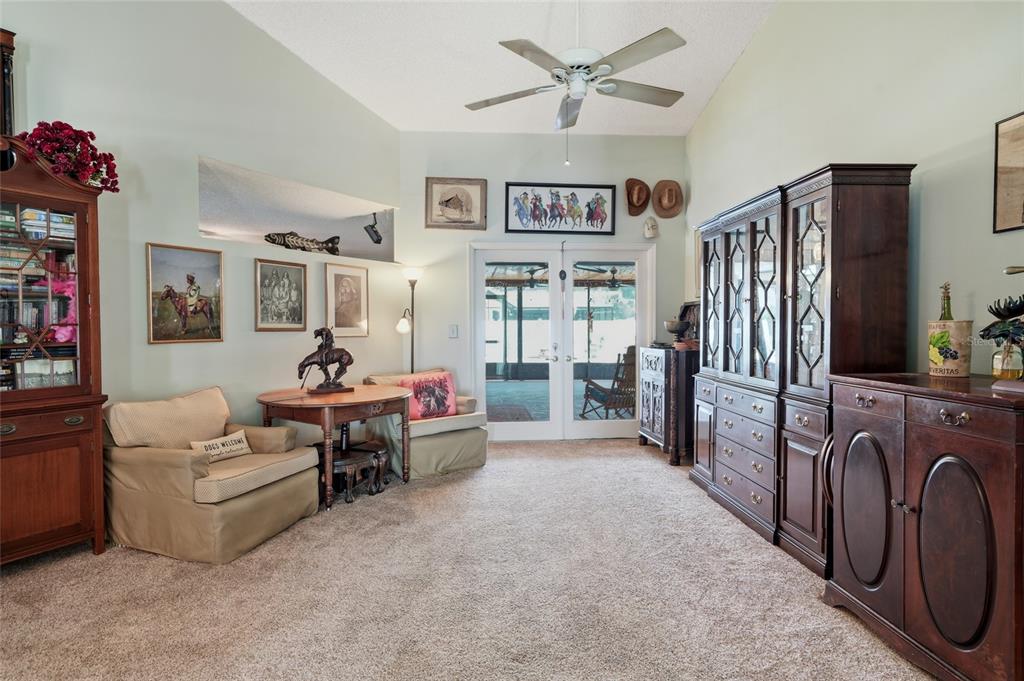A living room features beige carpet, a ceiling fan, wooden furniture, and glass double doors — 1150 WINDSOR WAY, LUTZ, FL