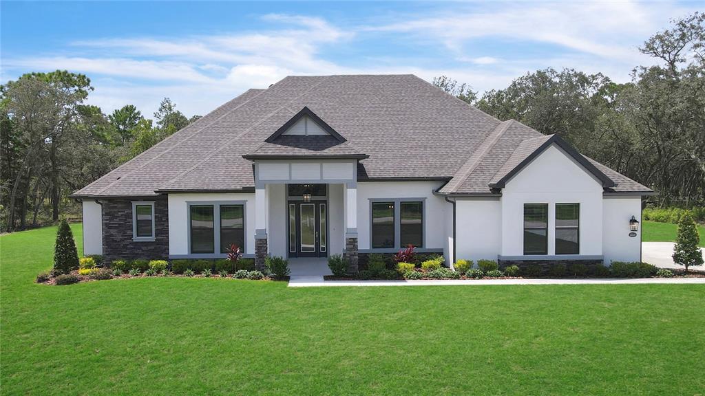 A single-story house exterior features white stucco walls, stone accents, and a covered front porch — 13510 HAFLINGER WAY, HUDSON, FL