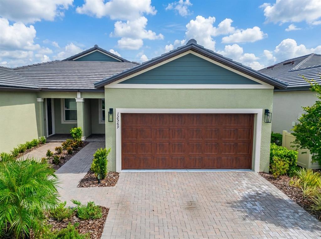 A single-story house features a green stucco exterior, a brown garage door, and a paved driveway — 12569 LILY QUARTZ LOOP, PARRISH, FL