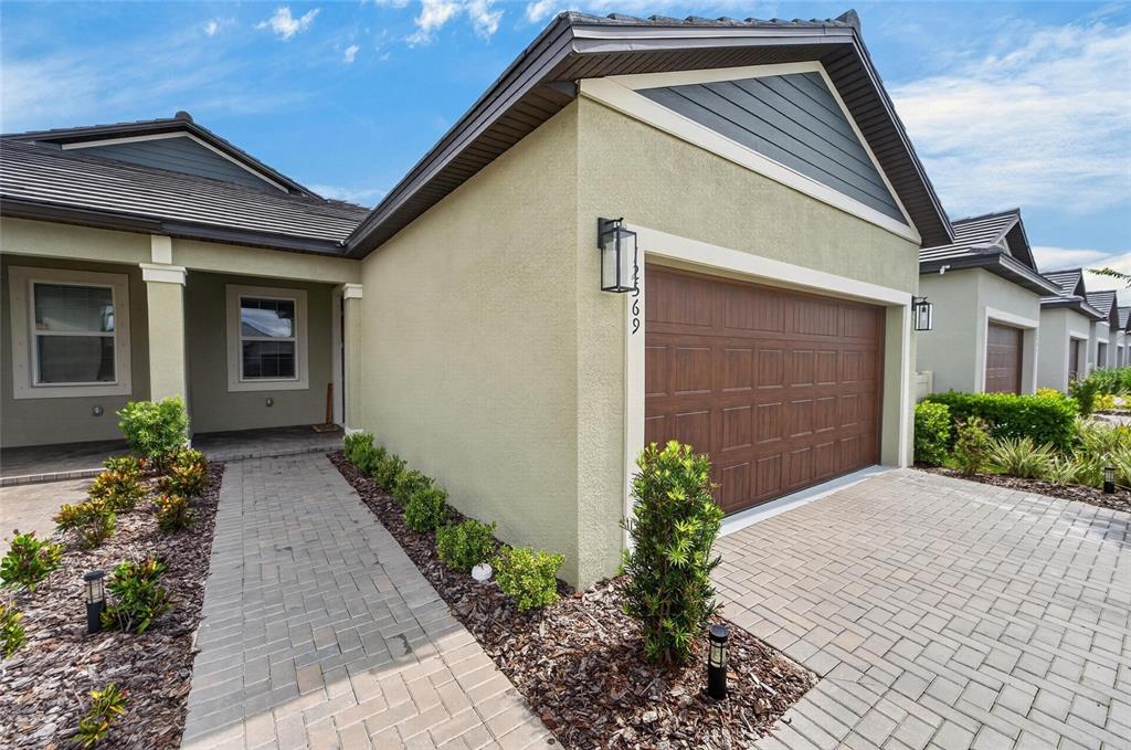 A single-story house exterior features a paved walkway, a brown garage door, and landscaping — 12569 LILY QUARTZ LOOP, PARRISH, FL