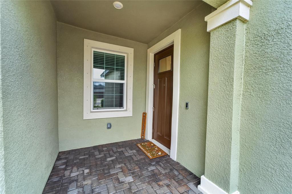 A covered front porch with a brown door, a window, and brick paver flooring — 12569 LILY QUARTZ LOOP, PARRISH, FL