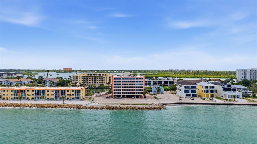 An aerial view shows beachfront apartment buildings along a coastline with a rocky shoreline — 9150 BLIND PASS ROAD UNIT 206, SARASOTA, FL