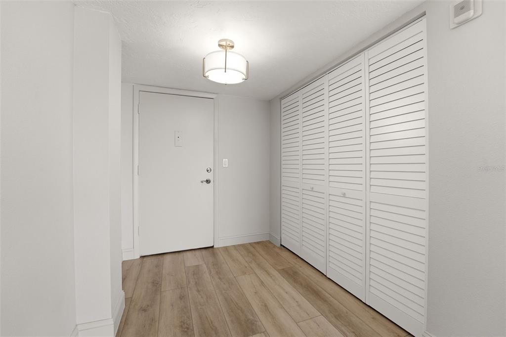 A spacious living room with light wood-look flooring, a kitchen pass-through, and floor-to-ceiling windows — 9150 BLIND PASS ROAD UNIT 206, SARASOTA, FL