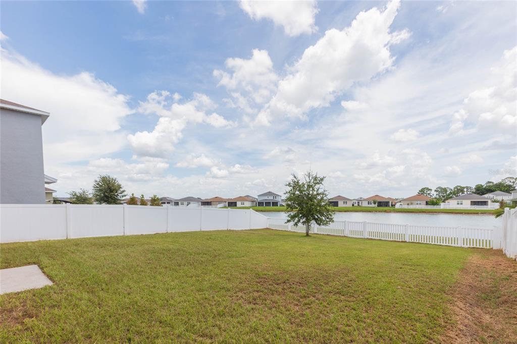 A grassy backyard features a white vinyl fence, a small tree, and a pond view — 478 AUTUMN STREAM DRIVE, AUBURNDALE, FL