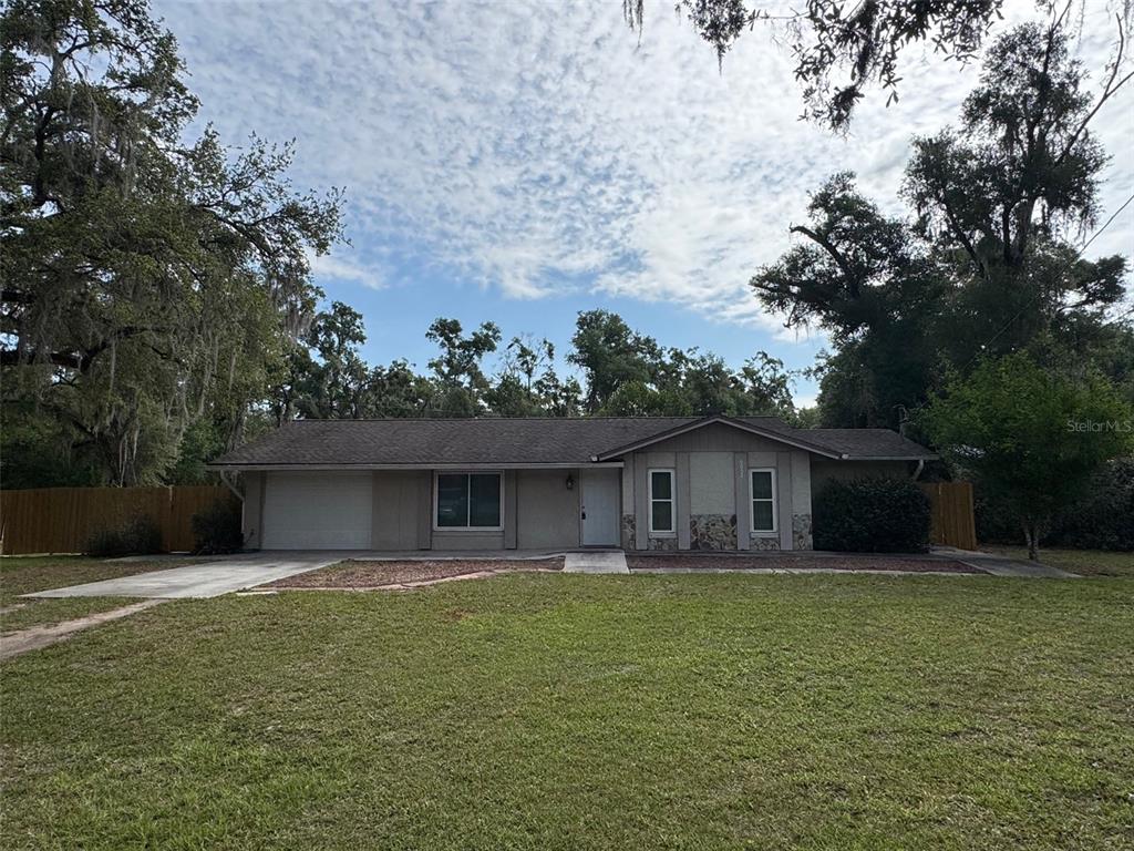 A single-story house with a garage, stone accents, and a large lawn under trees — 6052 IDLE A WHILE CIRCLE, DADE CITY, FL