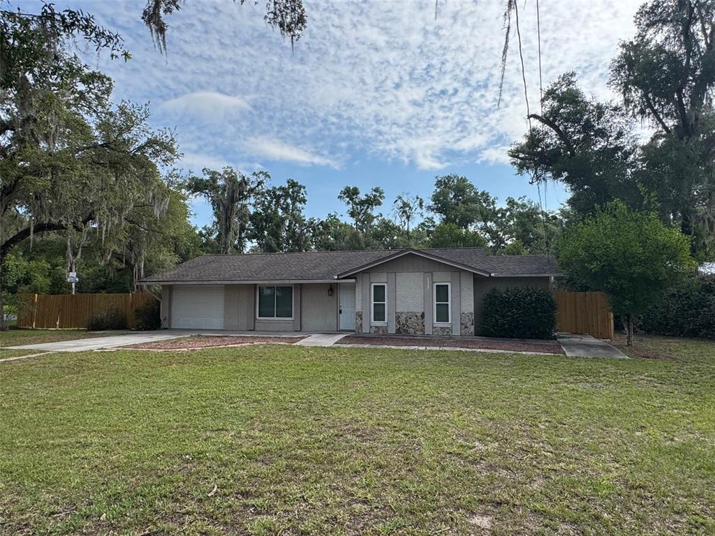 A single-story house with a garage, stone accents, and a large lawn under trees — 6052 IDLE A WHILE CIRCLE, DADE CITY, FL