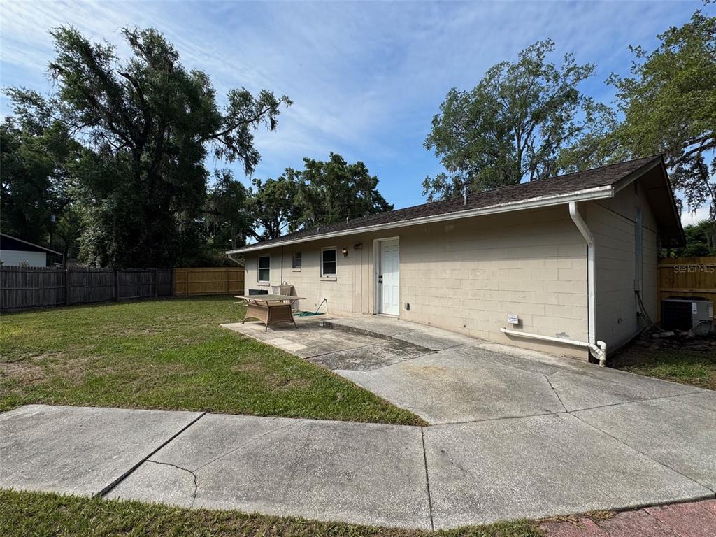 A beige concrete block house features a back patio, a white door, and a yard — 6052 IDLE A WHILE CIRCLE, DADE CITY, FL