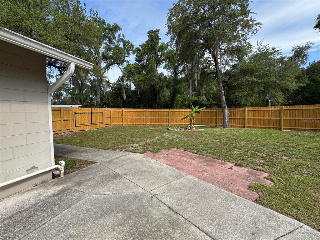 A backyard features a concrete patio, a small brick area, and a wooden privacy fence — 6052 IDLE A WHILE CIRCLE, DADE CITY, FL