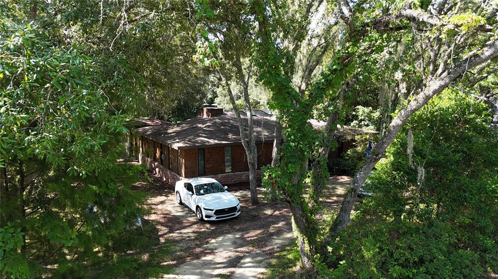 A white car is parked in the driveway of a brick house surrounded by trees — 34146 UMBRELLA ROCK DRIVE, WEBSTER, FL