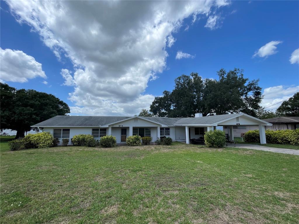 A single-story house with a white exterior, a carport, and a large front lawn — 879 S TERRACE DRIVE, EAGLE LAKE, FL