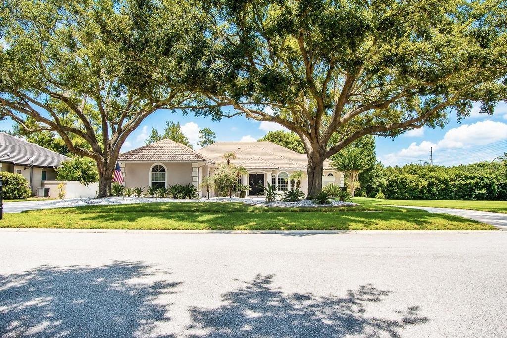 A single-story house with a tiled roof sits behind two large trees on a lawn — 9606 CAMBERLEY CIRCLE, ORLANDO, FL