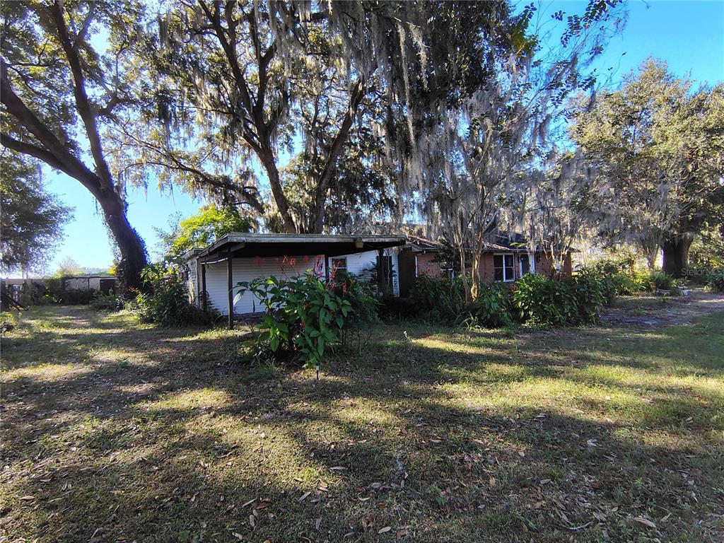 A single-story house with a carport sits on a grassy lot under large trees — 3537 E C 462, WILDWOOD, FL