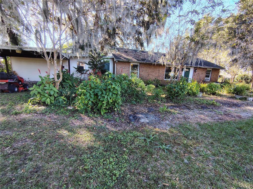 A single-story brick house with a carport and overgrown landscaping under large trees — 3537 E C 462, WILDWOOD, FL