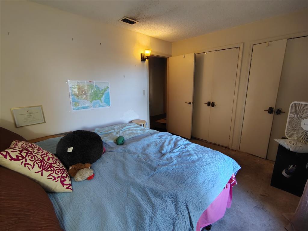 A bedroom features a bed with a blue quilt, two closet doors, and a ceiling vent — 3537 E C 462, WILDWOOD, FL