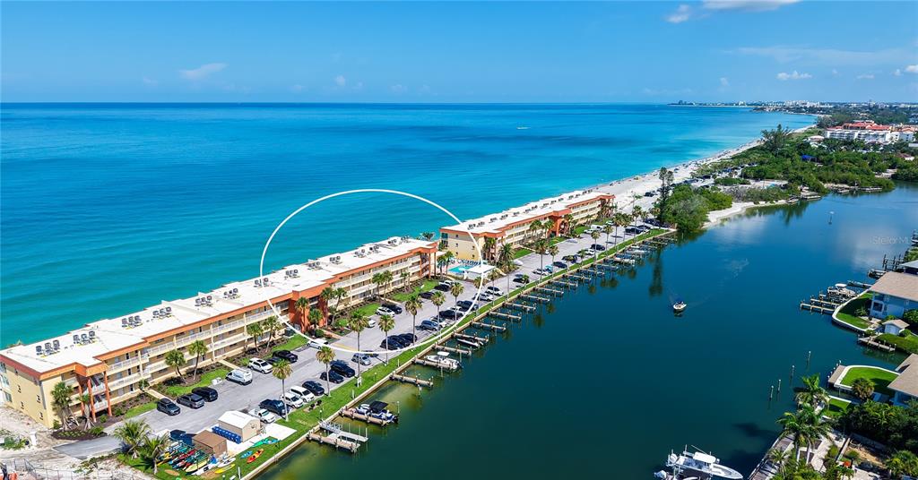 An aerial view shows a long, multi-story apartment building situated between the ocean and a canal — 9000 BLIND PASS ROAD UNIT 303, SARASOTA, FL