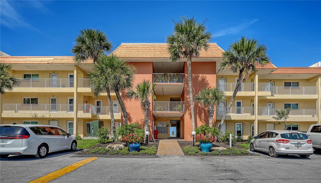 A three-story apartment building with a peach-colored center section, palm trees, and parking lot — 9000 BLIND PASS ROAD UNIT 303, SARASOTA, FL