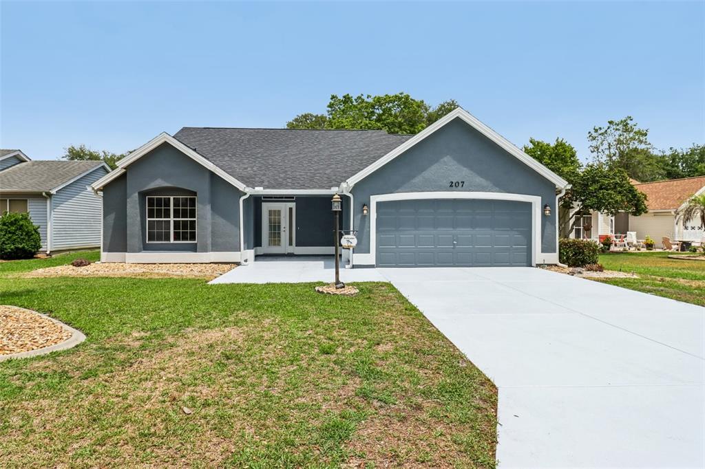 A covered concrete entryway leads to a white double door on a blue house — 207 DESOTA COURT, THE VILLAGES, FL