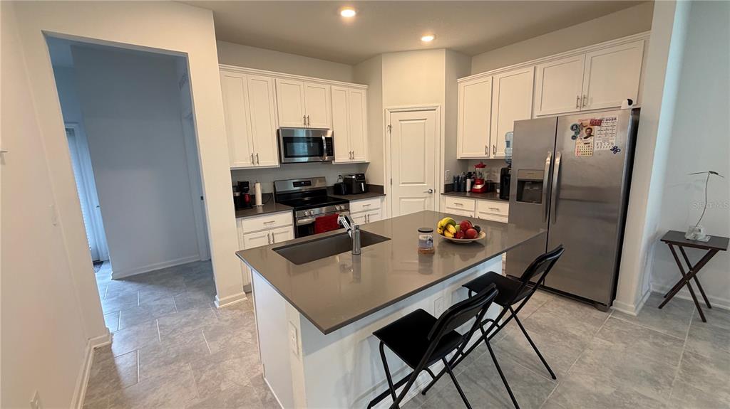 A kitchen features white cabinets, stainless steel appliances, a gray island, and tile flooring — 4125 PINO STREET, APOPKA, FL