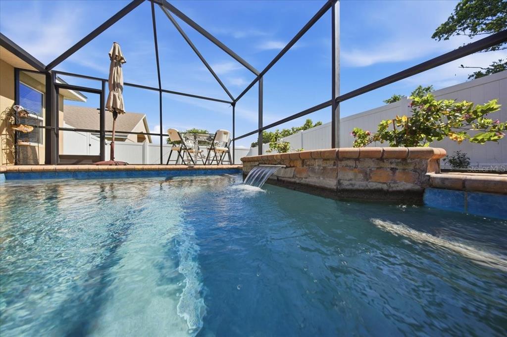 A swimming pool with a stone water feature inside a screened-in lanai — 1408 LEGATTO LOOP, DUNDEE, FL