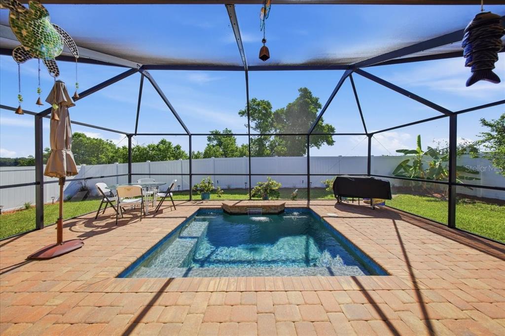 A screened-in patio features a small rectangular swimming pool with a stone water feature — 1408 LEGATTO LOOP, DUNDEE, FL