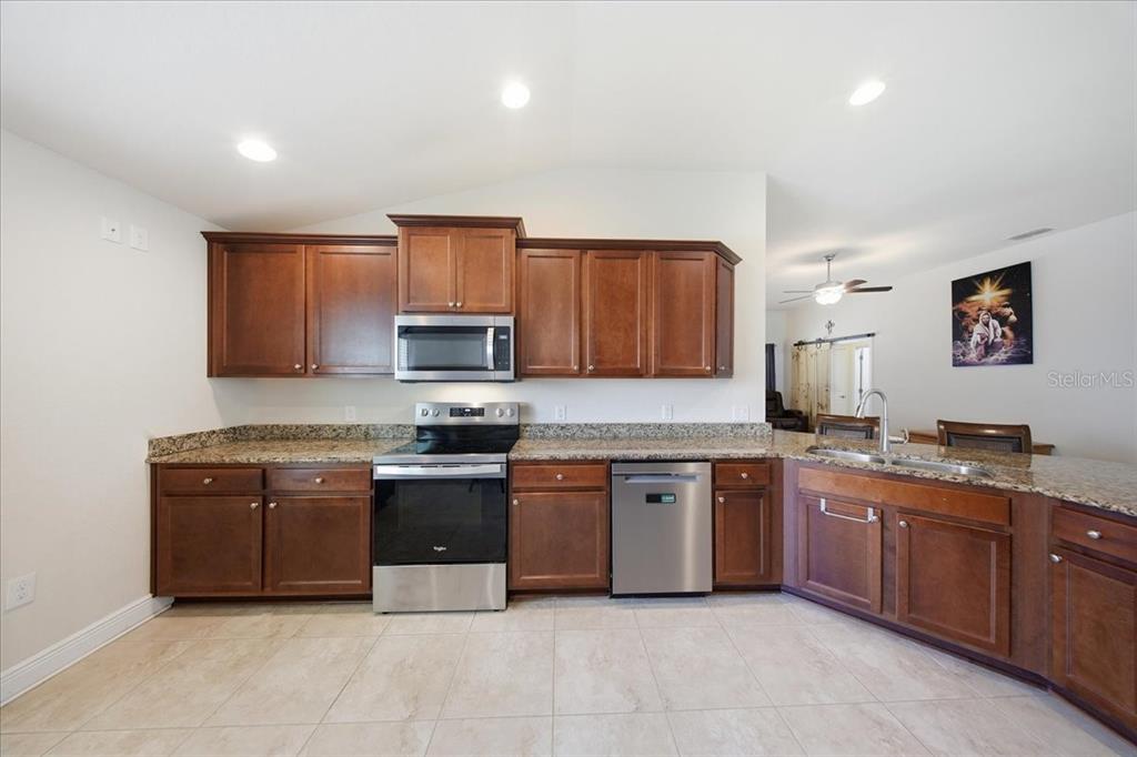 A kitchen features dark wood cabinets, stainless steel appliances, and granite countertops — 1408 LEGATTO LOOP, DUNDEE, FL