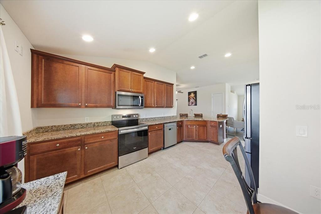 A kitchen features wood cabinets, granite countertops, stainless steel appliances, and light-colored tile flooring — 1408 LEGATTO LOOP, DUNDEE, FL