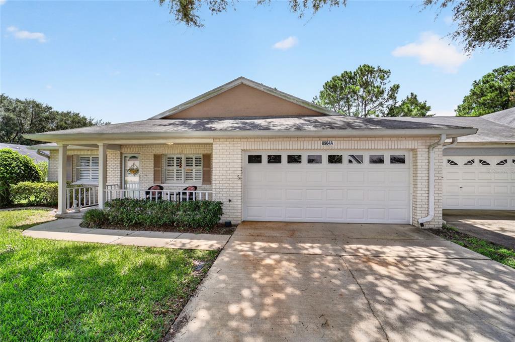 A covered brick porch features a white front door, a window with shutters, and two chairs — 8964 SW 95TH STREET UNIT A, OCALA, FL
