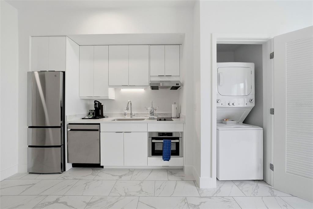 A small kitchen with white cabinets, stainless steel appliances, and a laundry closet with stacked units — 411 E SHORE DRIVE UNIT 514, CLEARWATER BEACH, FL