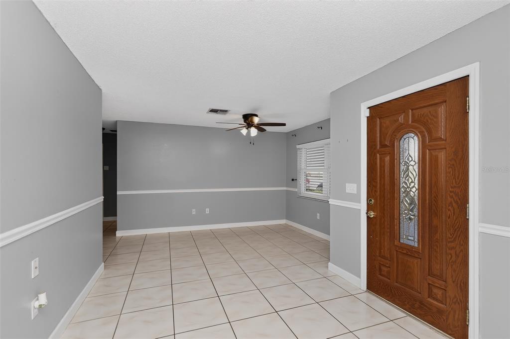 An entryway with light-colored tile flooring, gray walls, white chair rail molding, and a wooden door — 3104 DOLE STREET, HOLIDAY, FL