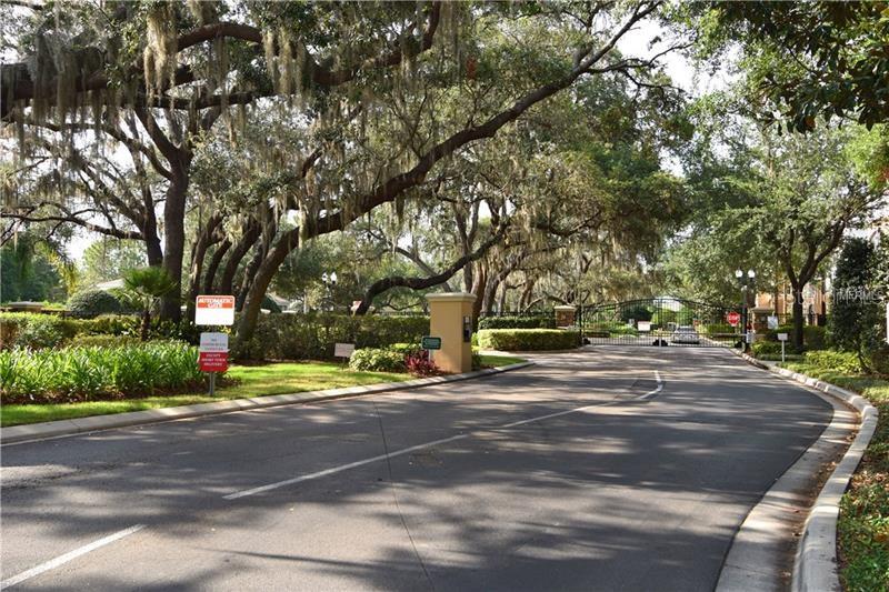 A paved road leads to a gated community entrance shaded by large, moss-covered oak trees — 6214 STEVENSON DRIVE UNIT 201, ORLANDO, FL