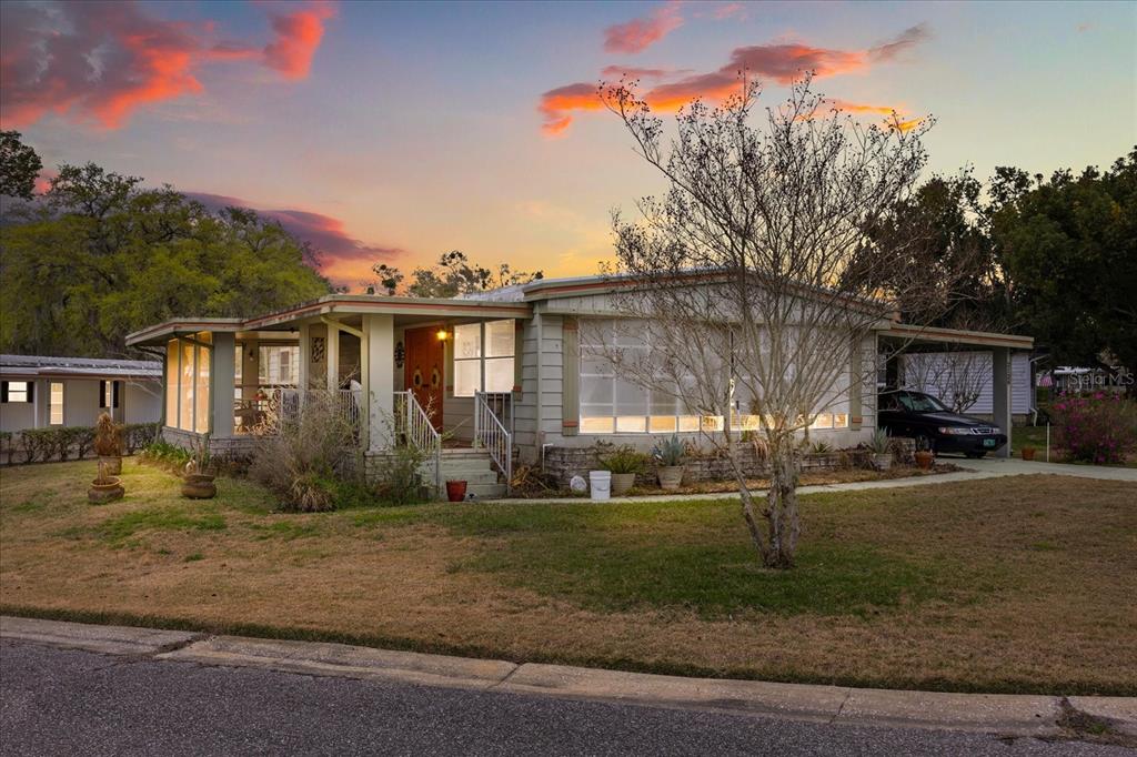 A single-story house with a front porch, large windows, and a carport at sunset — 2129 OAK GROVE DRIVE UNIT 58, ZELLWOOD, FL