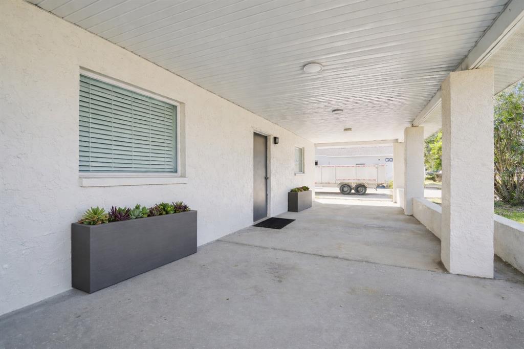 A covered concrete patio features white stucco walls, a gray door, and two rectangular planters — 6010 WALL STREET, PORT RICHEY, FL