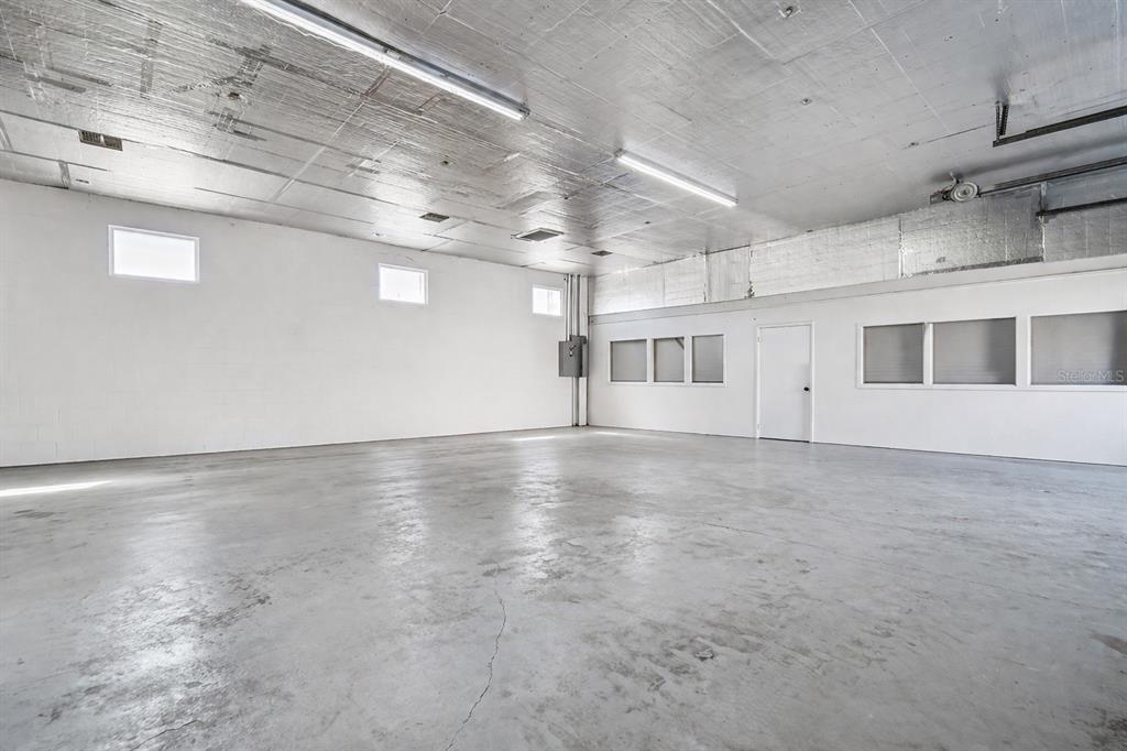 An empty industrial-style room features white block walls, a concrete floor, and reflective ceiling panels — 6010 WALL STREET, PORT RICHEY, FL