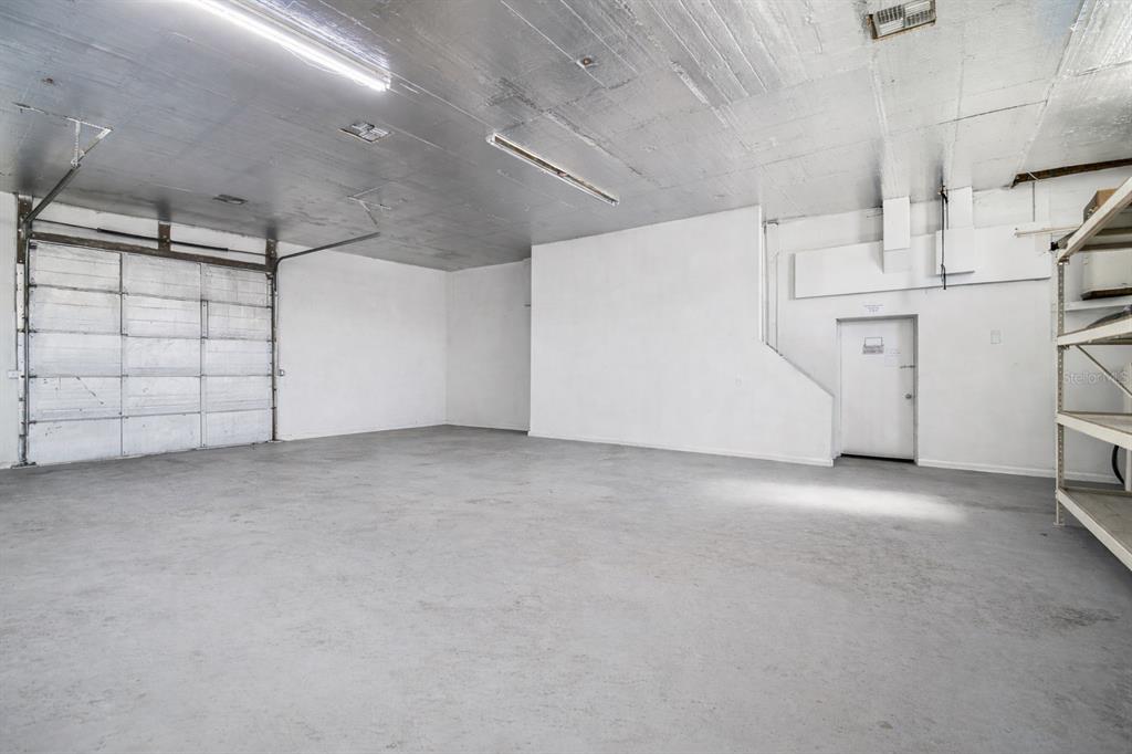 An empty industrial warehouse space with a concrete floor, metal ceiling, and roll-up door — 6010 WALL STREET, PORT RICHEY, FL