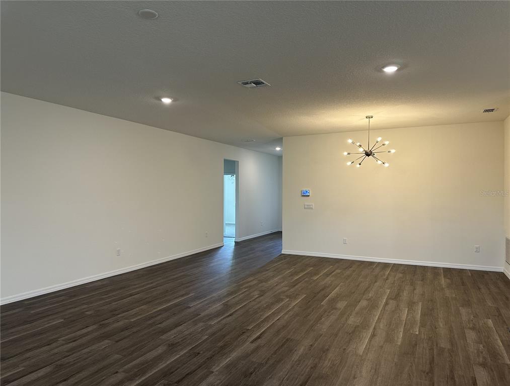 An empty room features dark wood-look flooring, white walls, recessed lighting, and a modern chandelier — 3272 ARCH AVENUE, ORMOND BEACH, FL
