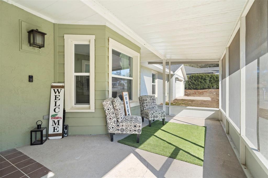 A screened-in porch features a concrete floor, two patterned chairs, and a green rug — 1049 W NEW YORK AVENUE, ORANGE CITY, FL