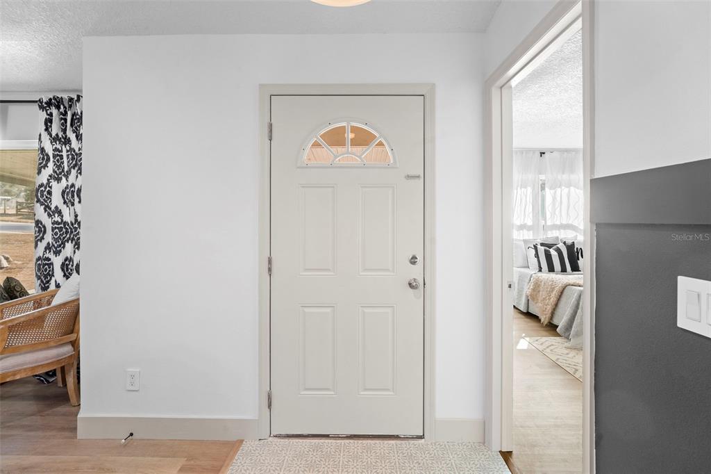 A white front door with a half-moon window opens into a room with light flooring — 1049 W NEW YORK AVENUE, ORANGE CITY, FL