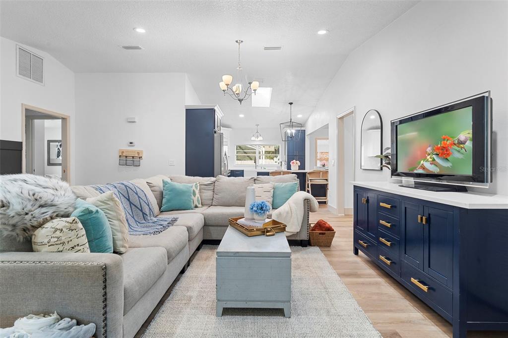 A living room features a gray sectional sofa, a blue media console, and an open kitchen — 1049 W NEW YORK AVENUE, ORANGE CITY, FL