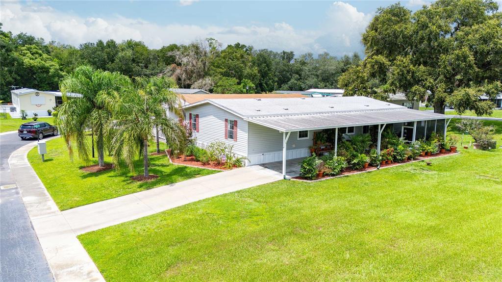 A light-colored manufactured home with a covered porch, concrete driveway, and palm trees — 38417 MONET DRIVE, ZEPHYRHILLS, FL