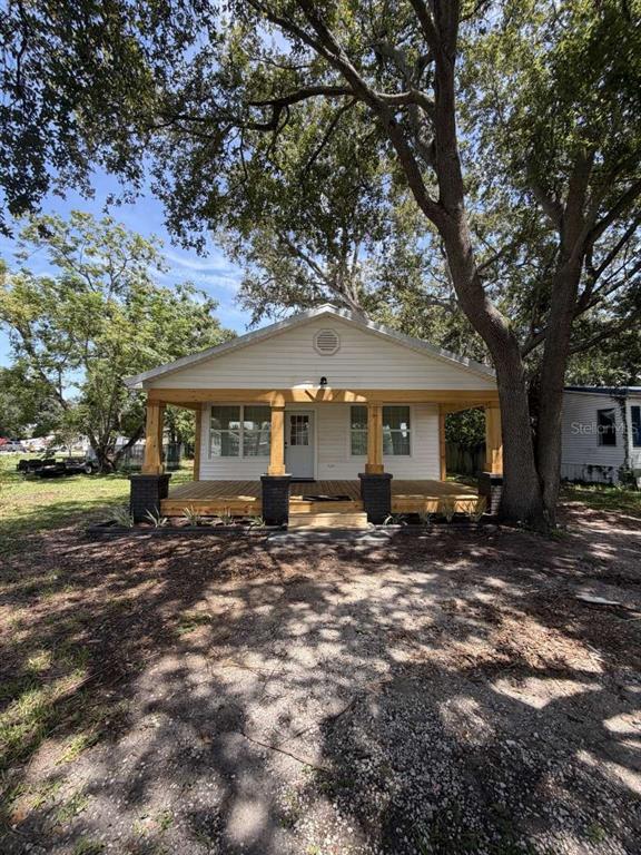A single-story house with white siding and a large wooden front porch under mature trees — 10120 ALAFIA STREET, GIBSONTON, FL