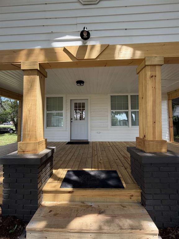 A wooden front porch features two brick-based columns and a white door with windows — 10120 ALAFIA STREET, GIBSONTON, FL
