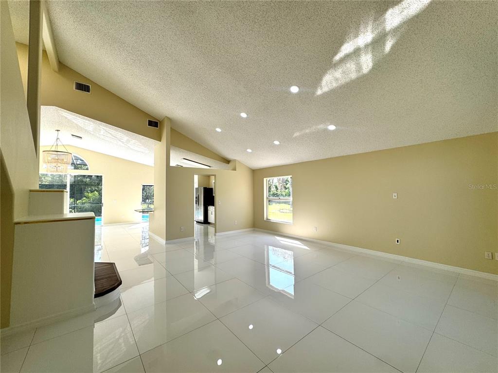A bright, open-concept living area features white tile flooring, vaulted ceilings, and recessed lighting — 2985 VISCOUNT CIRCLE, KISSIMMEE, FL