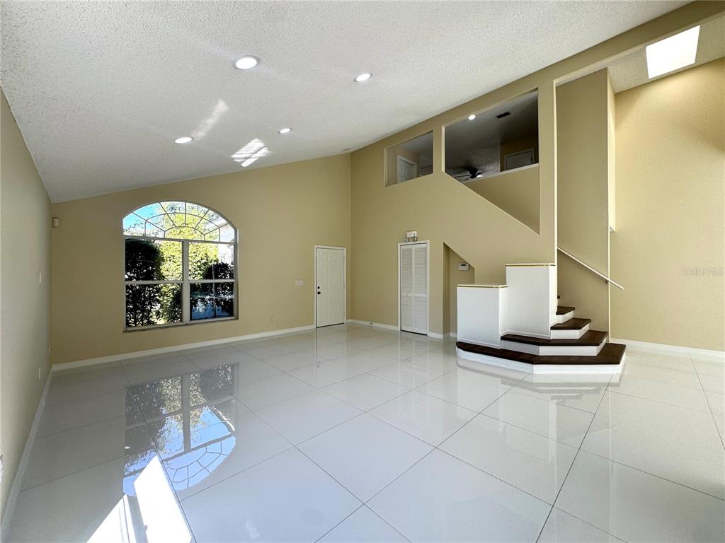 A spacious living room features high ceilings, white tile floors, and a staircase with dark treads — 2985 VISCOUNT CIRCLE, KISSIMMEE, FL