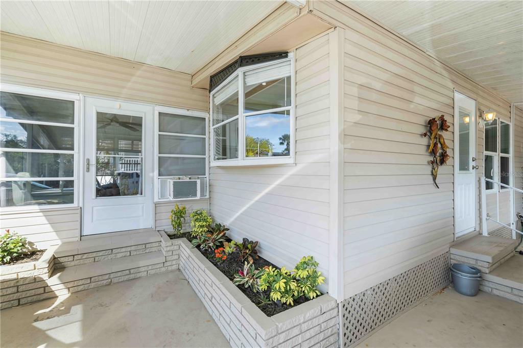 A covered patio features a brick planter box, light-colored vinyl siding, and two exterior doors — 10303 BURNT STORE ROAD UNIT 54, PUNTA GORDA, FL