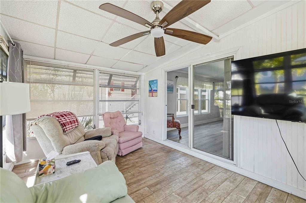 A sunroom features wood-look tile flooring, a ceiling fan, and a wall-mounted television — 10303 BURNT STORE ROAD UNIT 54, PUNTA GORDA, FL